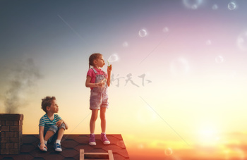 男孩女孩正在屋顶上看夕阳吹泡泡